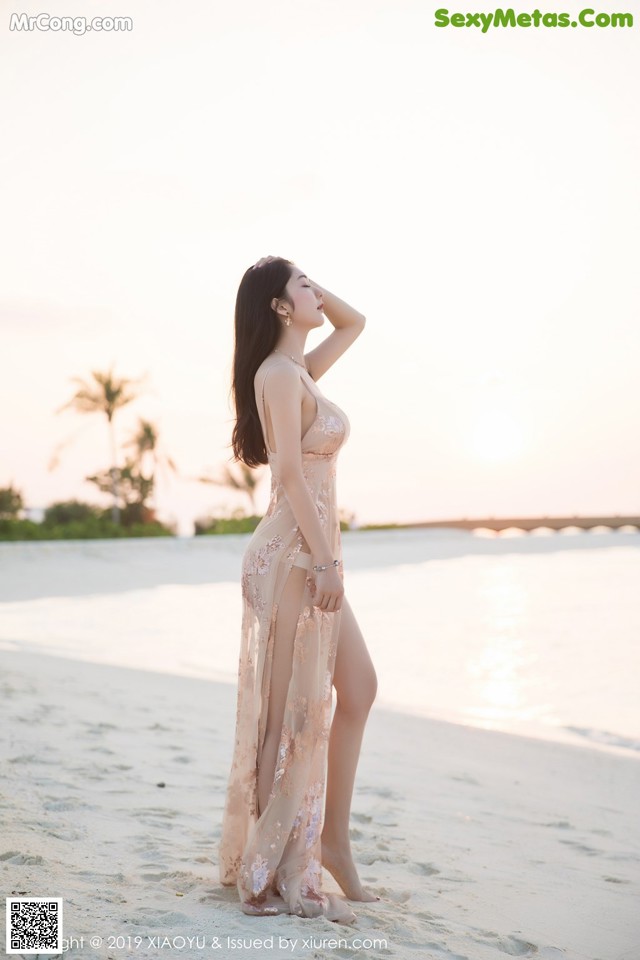 A woman in a long dress standing on a beach.