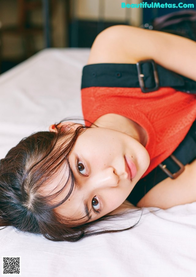 A woman laying on top of a bed wearing a red shirt.