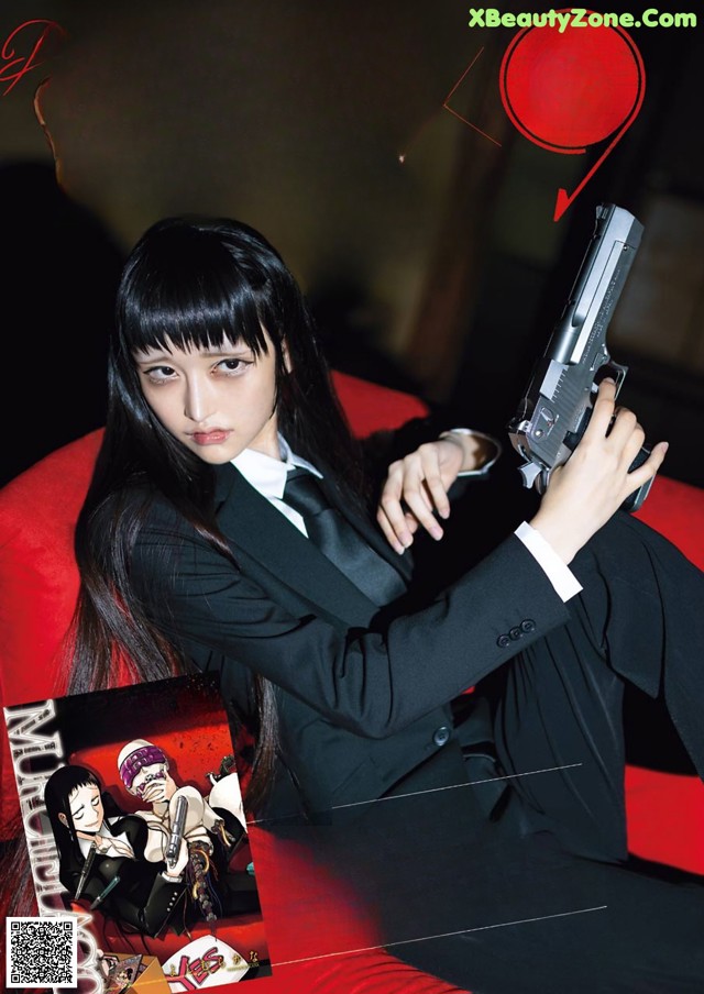 A woman in a suit holding a gun on a red couch.