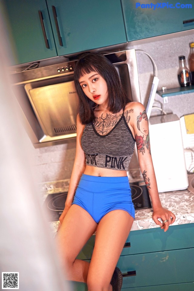 A woman in a black and white top and blue shorts posing in a kitchen.