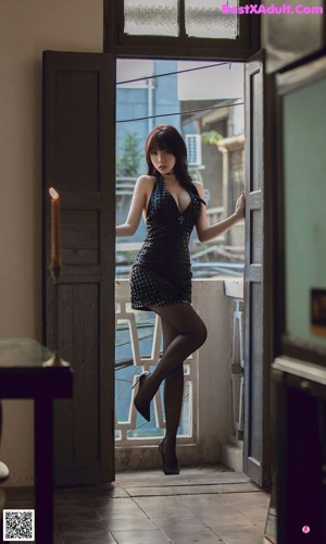 A woman in a black dress and high heels posing on a balcony.