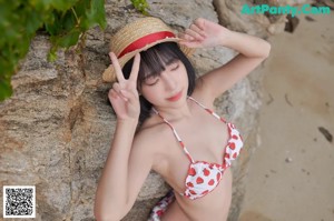 A woman in a bikini and straw hat posing on a rock.