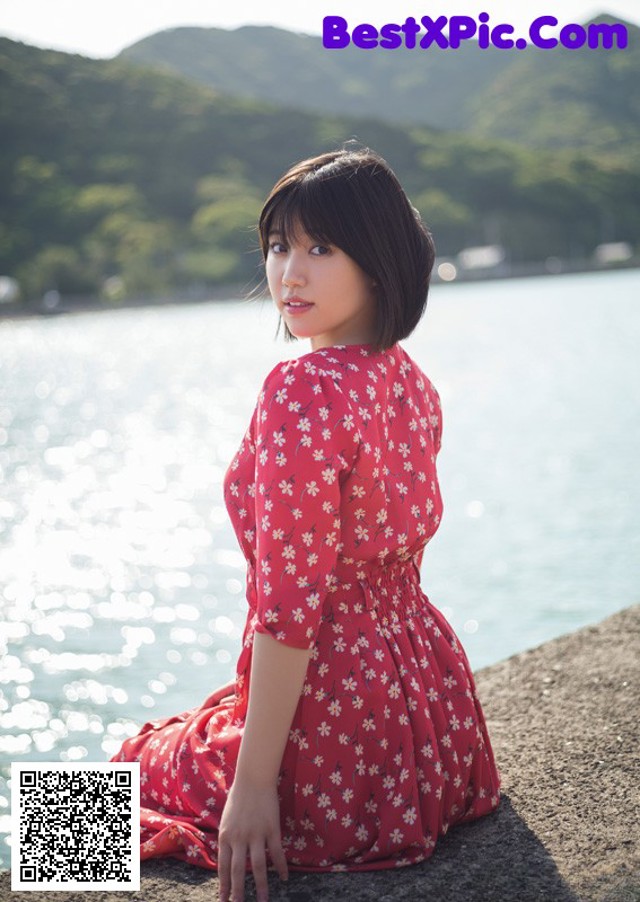 A woman in a red dress sitting by the water.