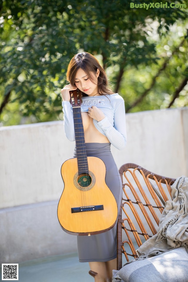 A woman holding a guitar while standing next to a couch.