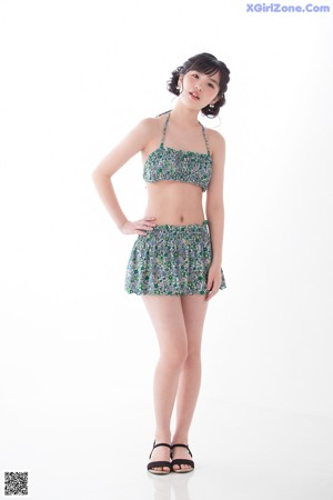 A woman in a bikini top and skirt leaning against a wall.