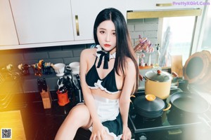 A woman in a maid outfit sitting on a kitchen counter.