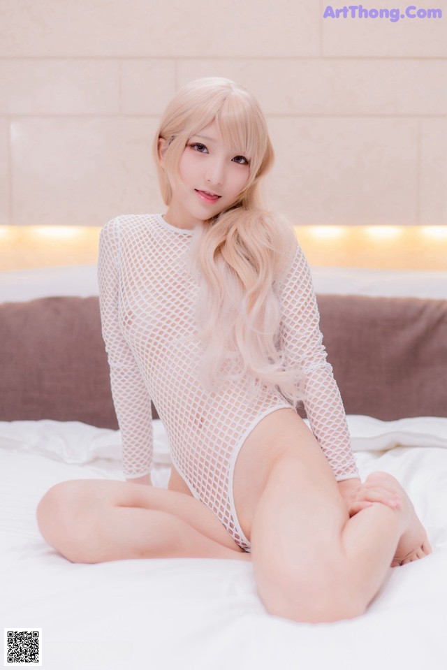 A woman in a white bodysuit sitting on a bed.