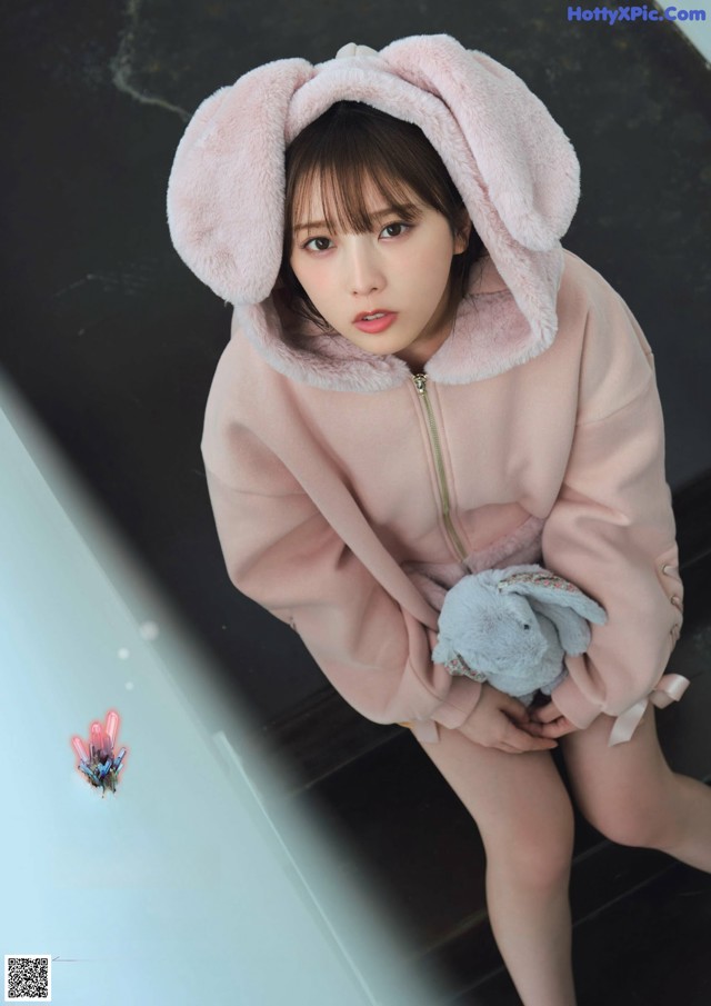A woman in a pink bunny costume holding a stuffed animal.