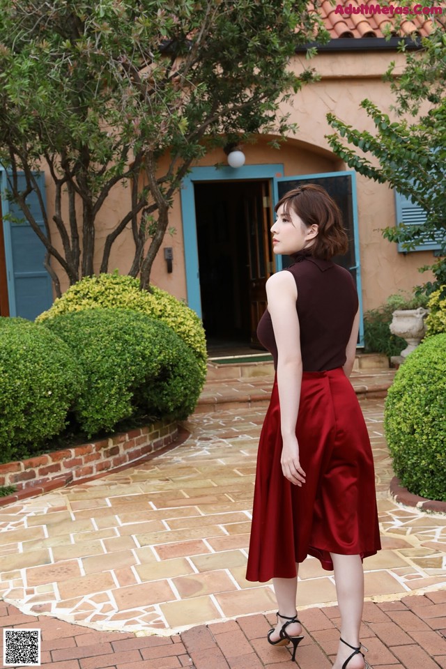 A woman in a red skirt is standing in front of a house.