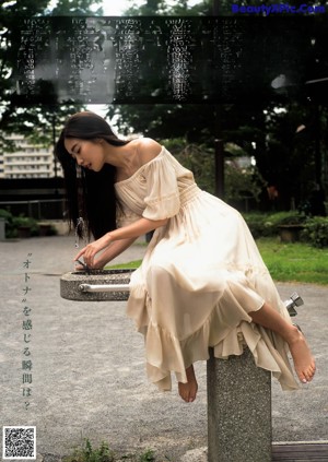 A woman in a black dress leaning on a railing by the water.