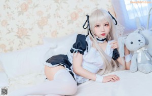 A woman in a maid outfit sitting on a bed.