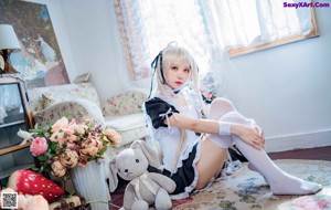 A woman in a maid outfit sitting on a bed with a stuffed animal.