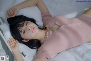 A woman in a pink bodysuit sitting on a bed.