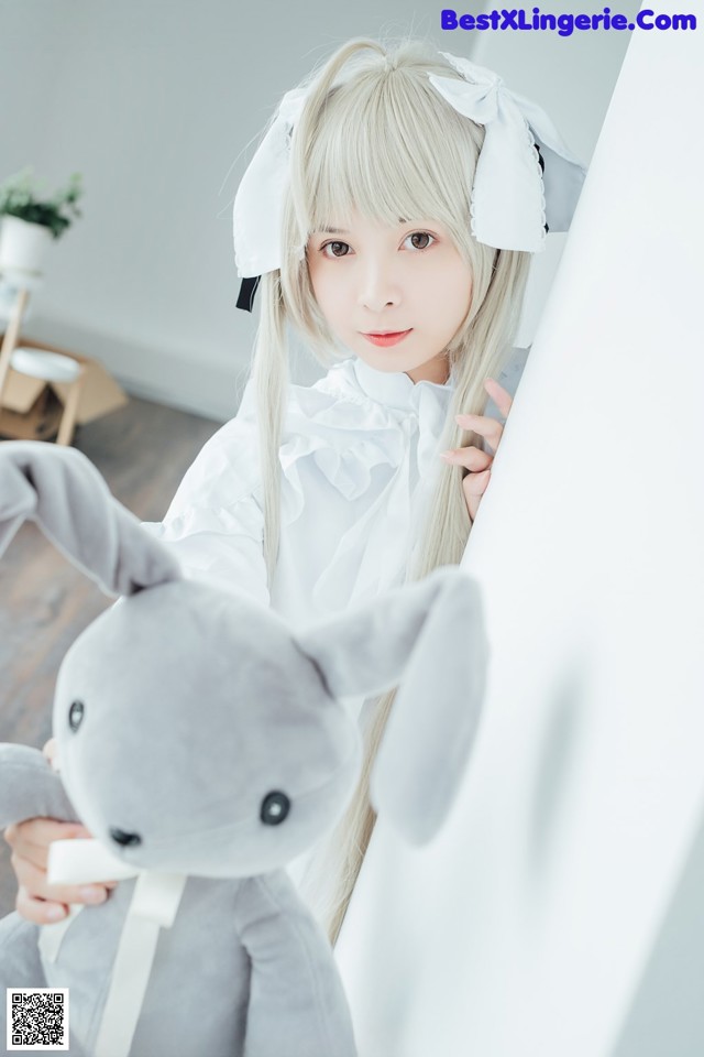 A girl in a white dress holding a gray stuffed animal.