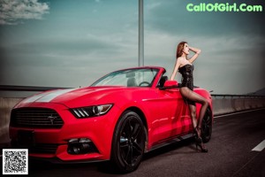 A woman leaning on the hood of a red car.