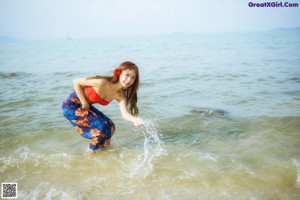 A woman standing in the ocean holding a straw hat.