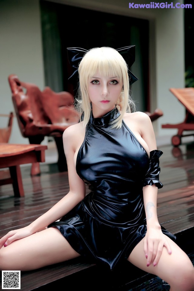 A woman in a black dress sitting on a wooden floor.