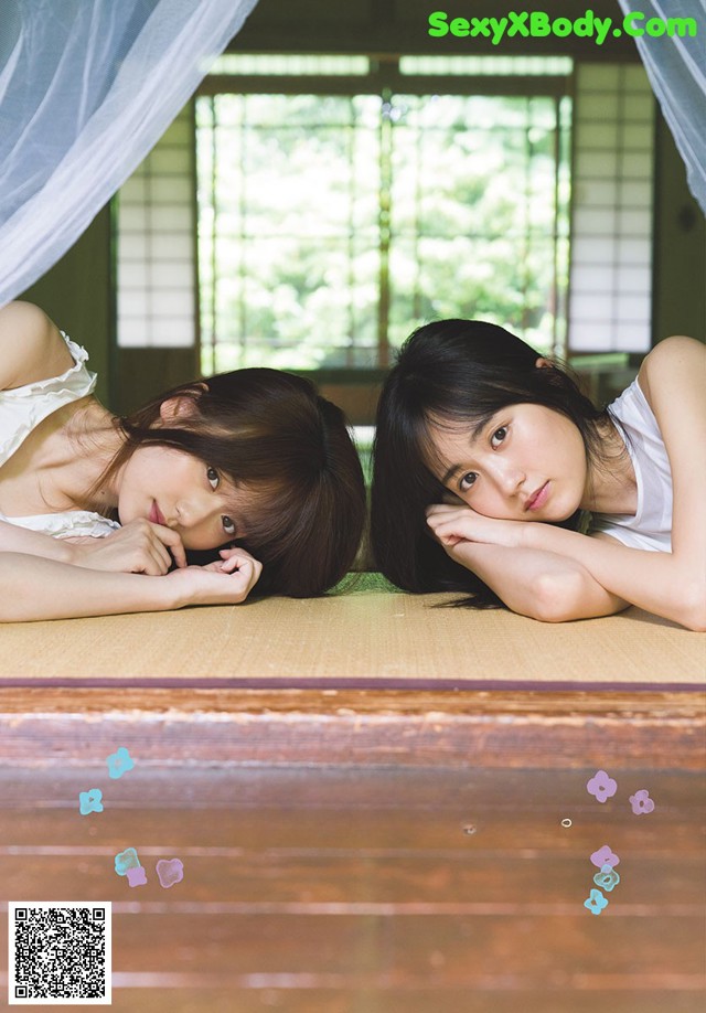 A couple of young women laying on top of a bed.