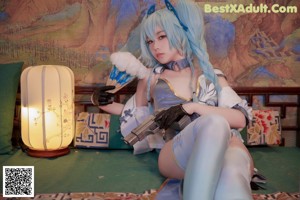 A woman with long blue hair sitting on a bed.